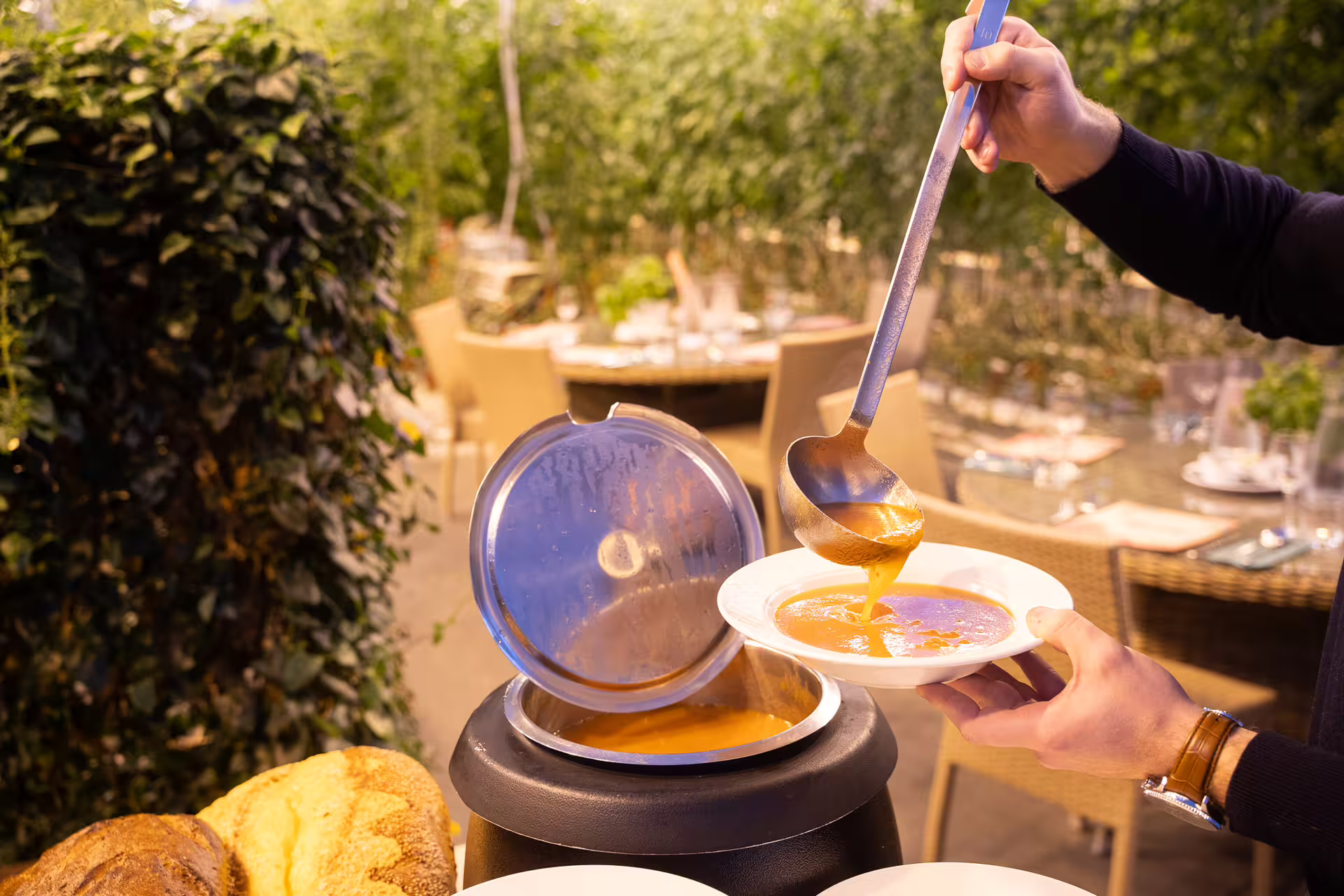 Server ladling golden tomato soup into white bowl at outdoor gourmet dining experience