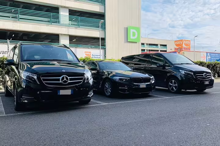 Fleet of luxury black Mercedes vans and BMW sedan at airport parking for private Frankfurt Airport round-trip transfers.