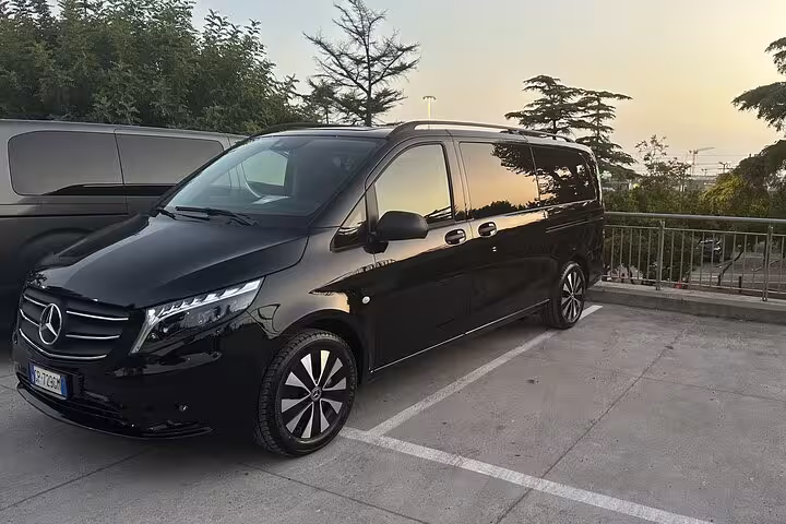 Luxury black Mercedes van for private transfer from Rome to Amalfi Coast, parked at sunset with scenic view.