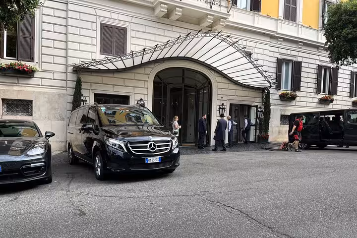 Luxury Mercedes van ready for private transfer from Milan to Courchevel, parked outside elegant hotel entrance.