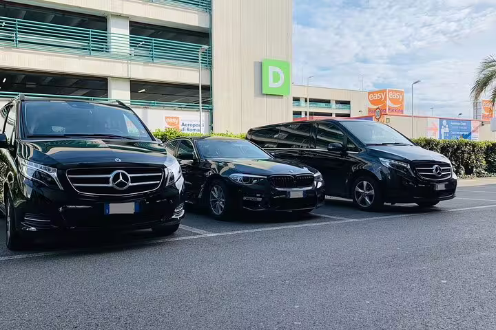 Three black luxury Mercedes vans and BMW sedan parked at airport terminal for private Milan to Malpensa MXP transfer service