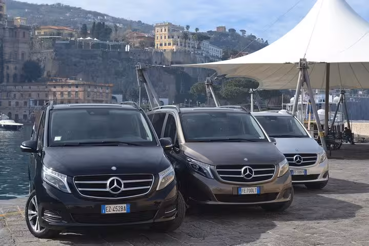 Fleet of luxury Mercedes vans ready for private transfer from Naples to Sorrento, parked by the coast.