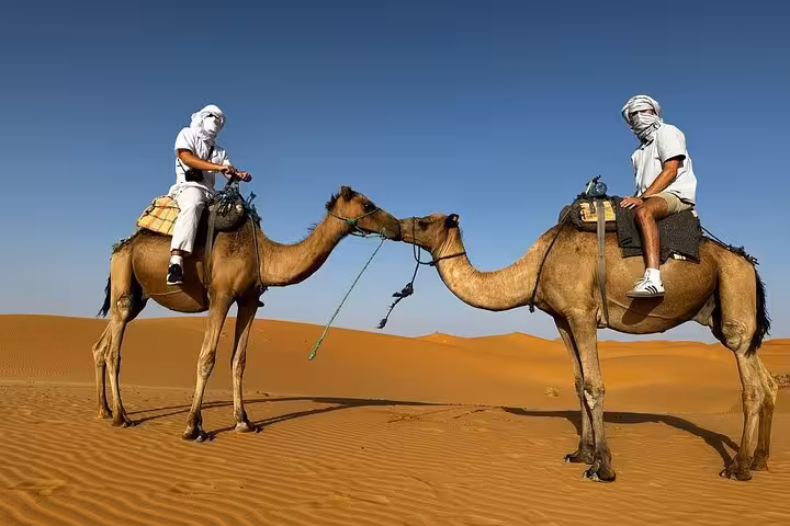 Two travelers on camels in the Moroccan desert, enjoying the scenic views during a luxury tour from Fes to Fes.
