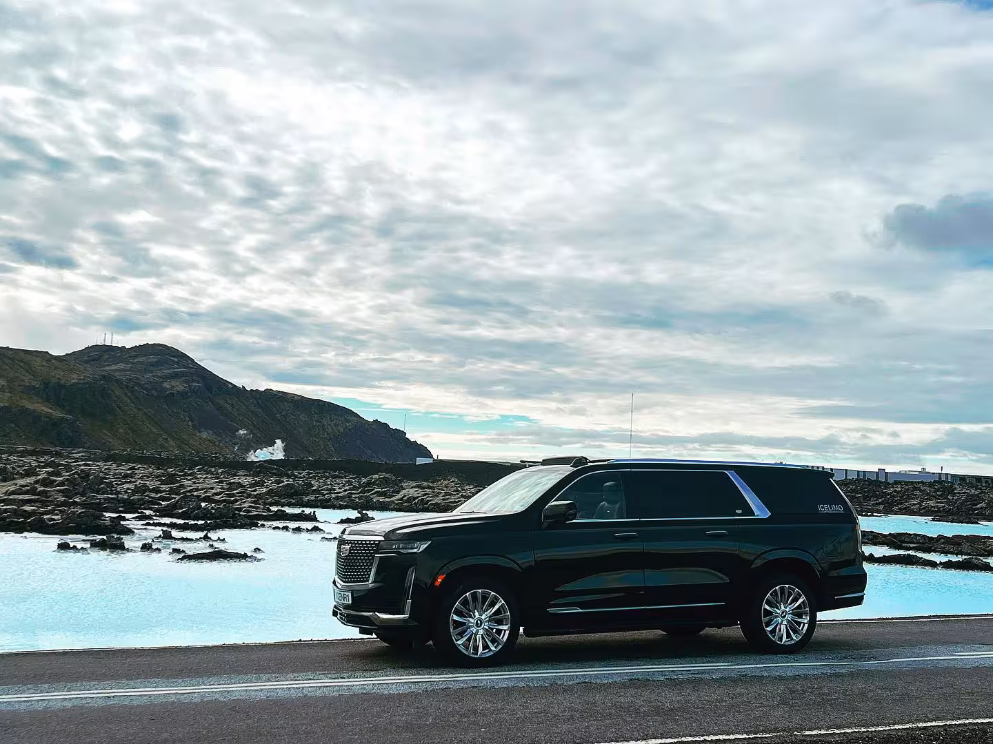 Black Cadillac Escalade luxury SUV parked beside the Blue Lagoon geothermal waters in Iceland