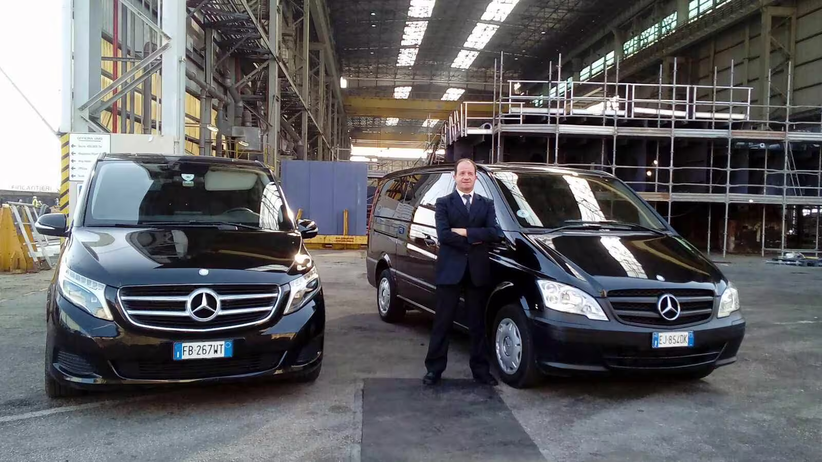 Chauffeur standing between luxury Mercedes vans offering private transfer from Naples to Benevento with premium service