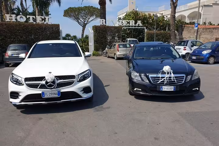 Elegant white and black luxury cars adorned with decorations, parked outside Hotel Riviera for a special occasion.