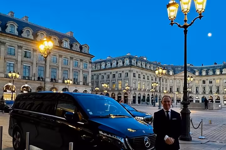 Chauffeur standing beside black Mercedes luxury van at Place Vendôme Paris at dusk