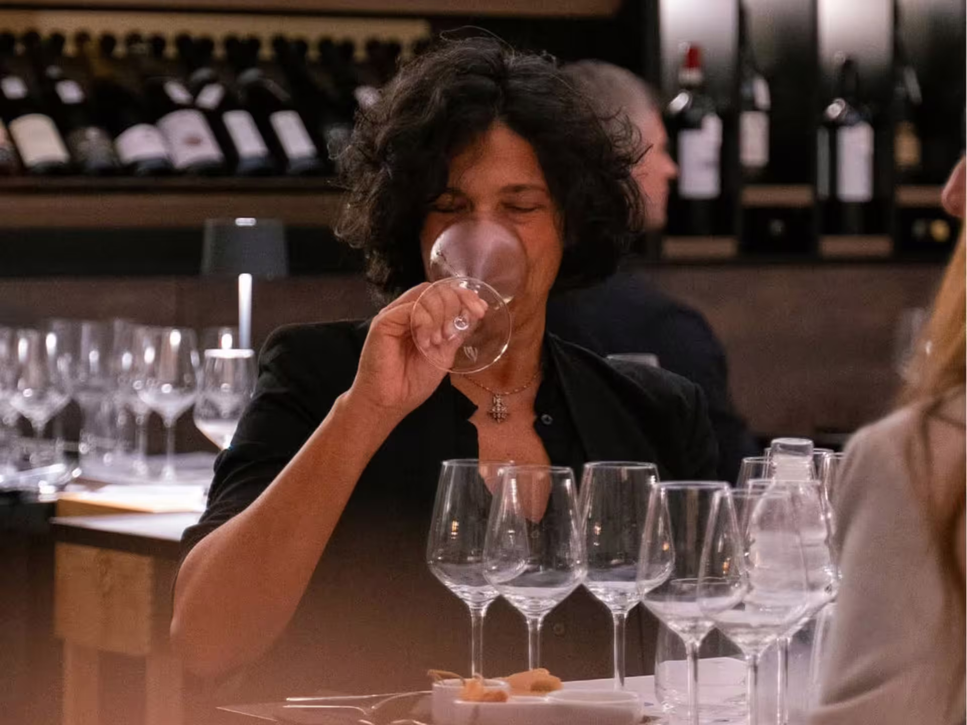 Guest sipping wine at a luxury Modena city center wine tasting, surrounded by glasses and bottle-lined shelves