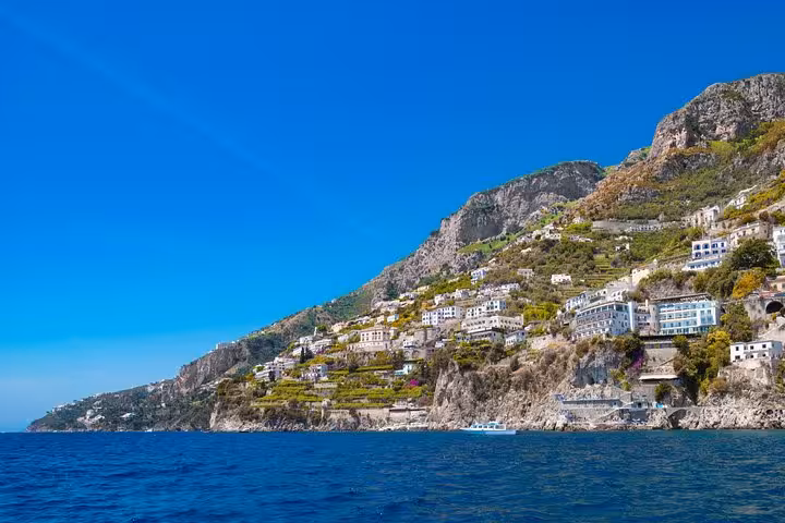 Scenic view of the Amalfi Coast's rugged cliffs and picturesque village from the sea under a clear blue sky.