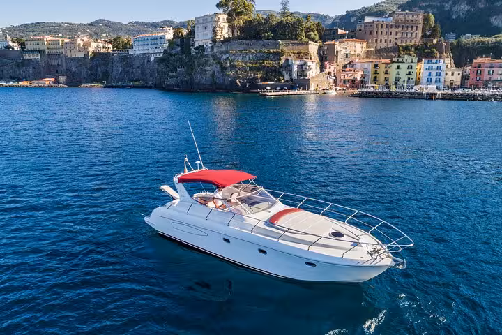 Luxury yacht Shamal 40 with red canopy cruising near Sorrento's vibrant coastline and historic architecture.