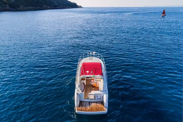 Rear view of a luxury yacht with red canopy, set against the serene waters of the Amalfi Coast near Sorrento.