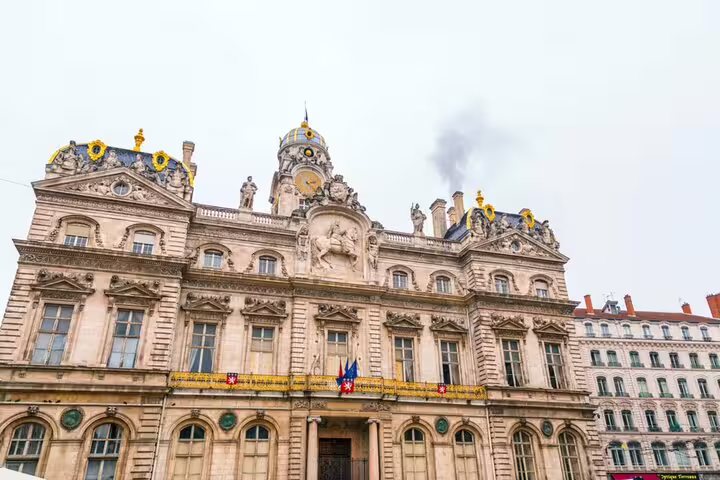 Ornate baroque facade of Lyon City Hall with clock tower, sculptures, and French flags on Place des Terreaux