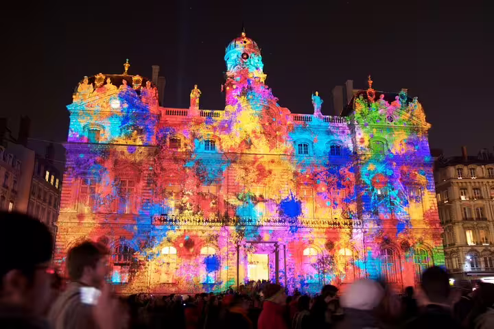 Colorful light projection on Lyon City Hall facade at night during Festival of Lights with crowd