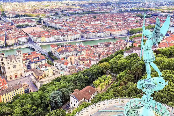 Aerial view of Lyon city with red rooftops, river Saône, and bronze angel statue on Fourvière basilica