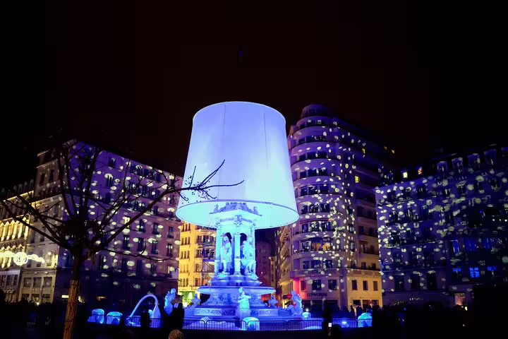 Giant illuminated lamp installation over Lyon fountain with colorful light projections on buildings at night