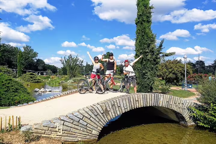Three cyclists posing with bikes on a stone arch bridge in a Lyon park on a sunny day
