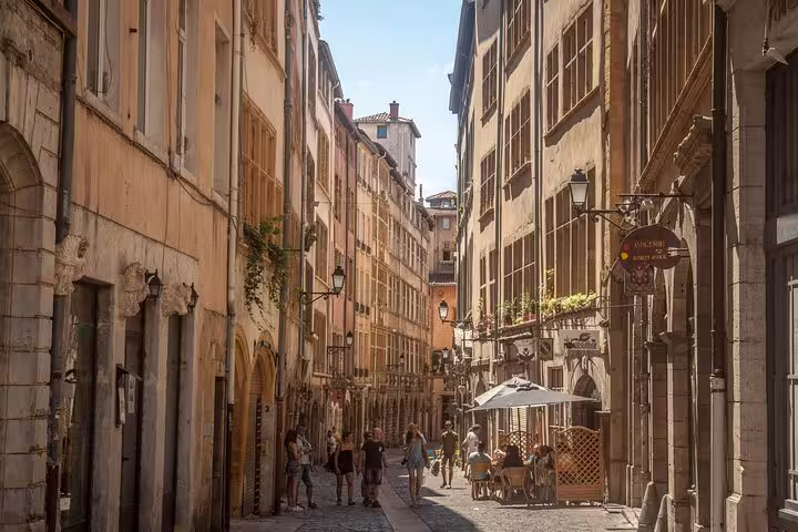 Narrow cobblestone street in Lyon's old quarter with pedestrians walking past historic buildings