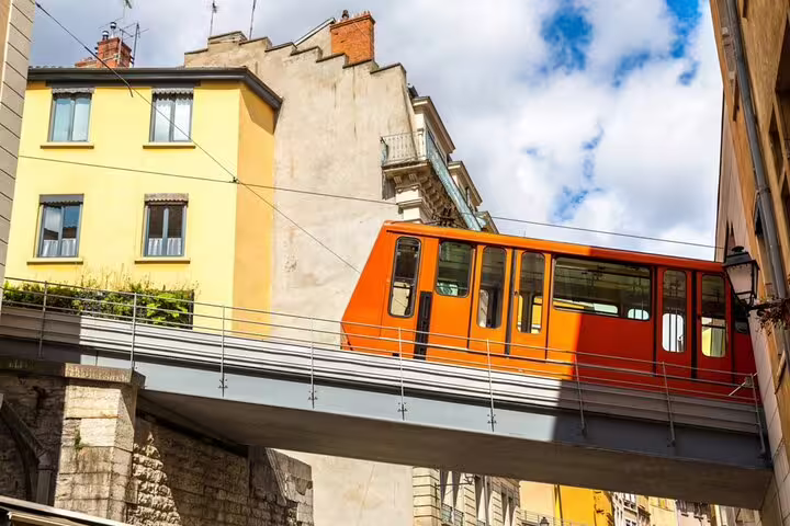 Orange funicular tram crossing elevated bridge between historic buildings in Lyon city center