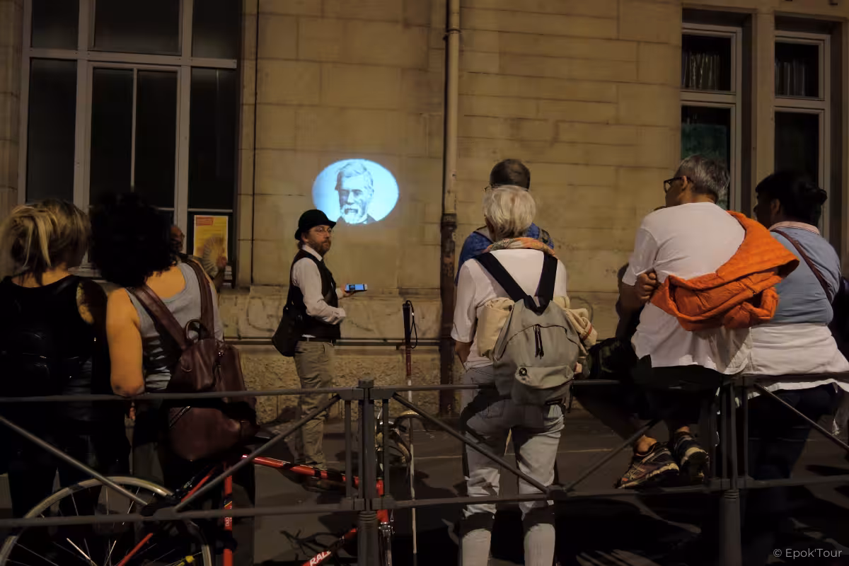 Tour guide projecting historical portrait on Lyon building wall at night for mystical walking tour