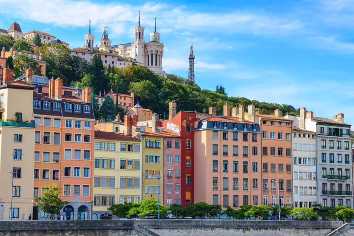 Colorful buildings along the Saône riverbank in Lyon with Fourvière Basilica on the hill