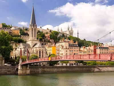 Lyon's Saône River with red footbridge, Gothic church spire, and Fourvière Basilica on hilltop above colorful Renaissance buildings