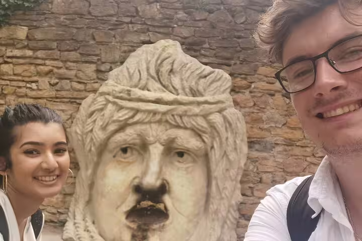 Two tourists smiling beside ancient Roman stone bust sculpture during walking tour in Lyon