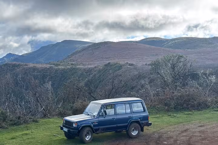 Classic 4x4 jeep parked at Madeira viewpoint with volcanic mountains and clouds on southwest island adventure