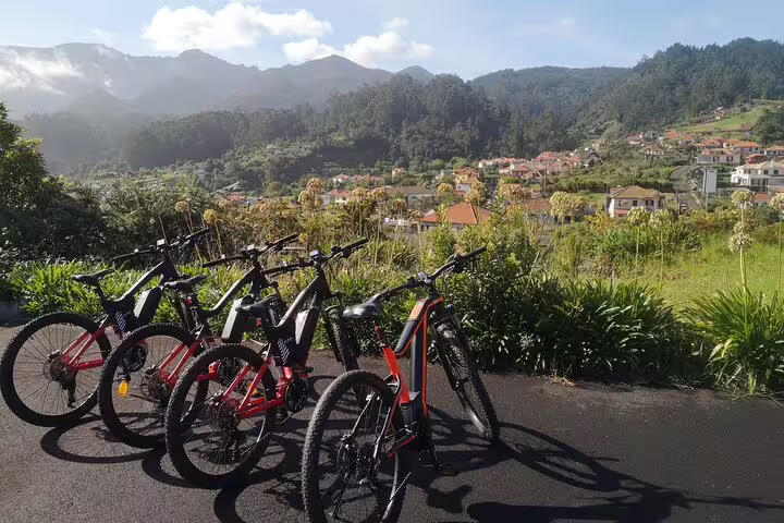 E-bikes ready for a guided tour on Madeira's lush north coast, showcasing scenic views of mountains and charming villages.
