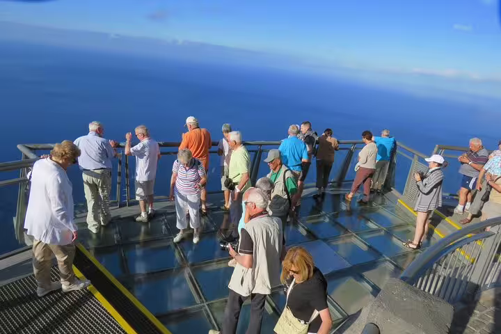 Tourists enjoy breathtaking views from Madeira's glass skywalk, surrounded by ocean vistas, capturing the island's untamed beauty.