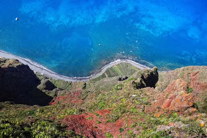 Aerial view of Madeira Island's dramatic coastline with vibrant blue ocean and terraced landscapes.