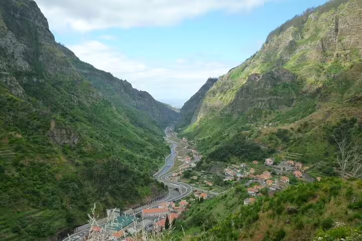 Scenic valley view in Madeira Island featuring winding roads and quaint villages nestled between towering green mountains.