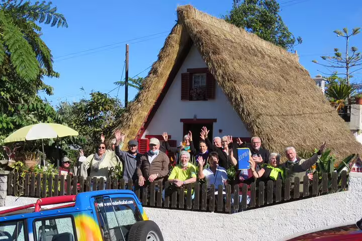 Tourists enjoying a sunny day at a traditional thatched house in Madeira, showcasing vibrant culture and scenic beauty.