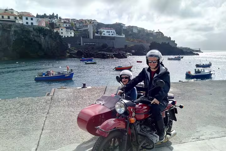 Tourists enjoy a scenic sidecar ride by the coastal village in Madeira, perfect for exploring with a unique perspective.