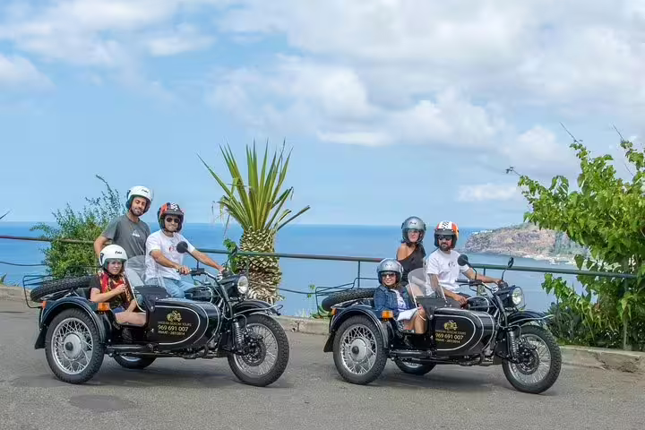 Tourists enjoy a scenic Madeira tour in classic sidecars with ocean views, perfect for a unique and thrilling island adventure.