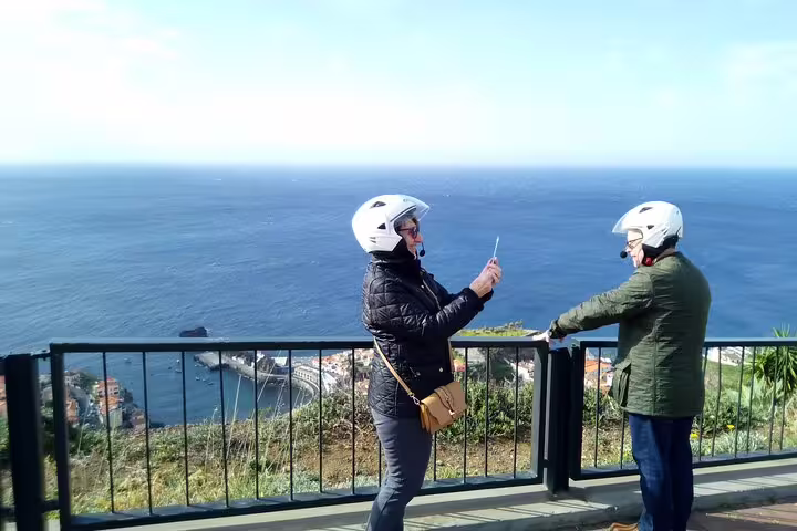 Two tourists in helmets enjoy a breathtaking ocean view on a Madeira scenic tour by sidecar and jeep.