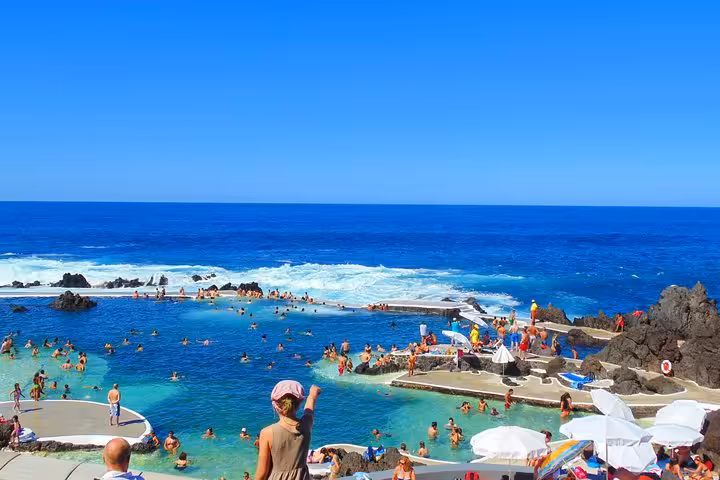 Tourists enjoying Madeira's scenic coastal natural lava rock pools with Atlantic Ocean waves on a guided tour