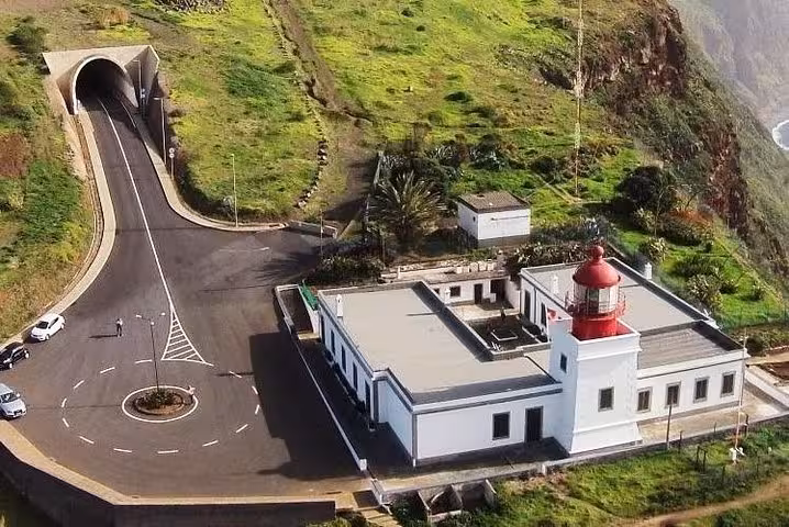 Aerial view of a white Madeira lighthouse with red dome near a scenic coastal tunnel on a guided highlights tour