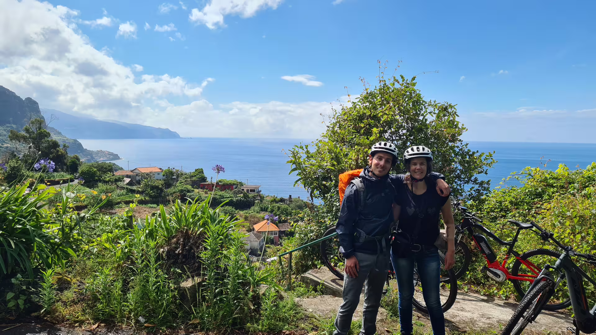 Couple enjoying a scenic e-bike tour along Madeira's stunning north coast with lush greenery and ocean views.
