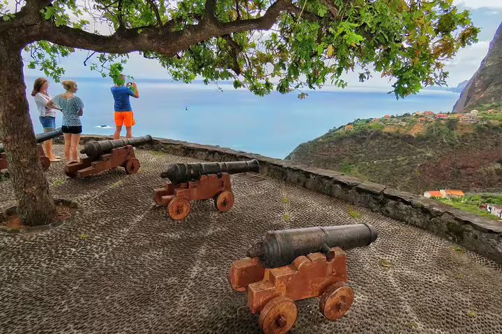 Tourists enjoy panoramic views of Madeira's coastline and historic cannons from a scenic viewpoint during the East Madeira Peaks & Santana shore excursion.