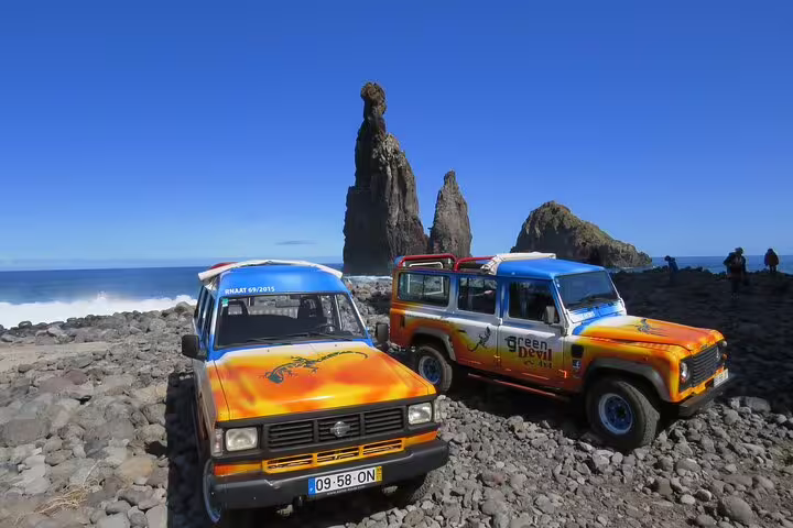 Colorful open-top jeeps on rocky Madeira coastline with dramatic sea stacks, promoting Enchanted Terraces & Fanal UNESCO tour.