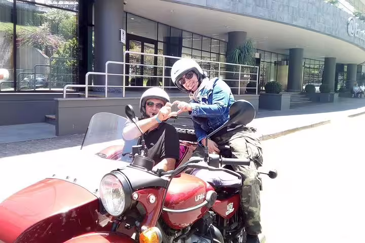 Tourists enjoy a thrilling Madeira Old Road West sidecar adventure, capturing smiles and excitement in front of a modern building.