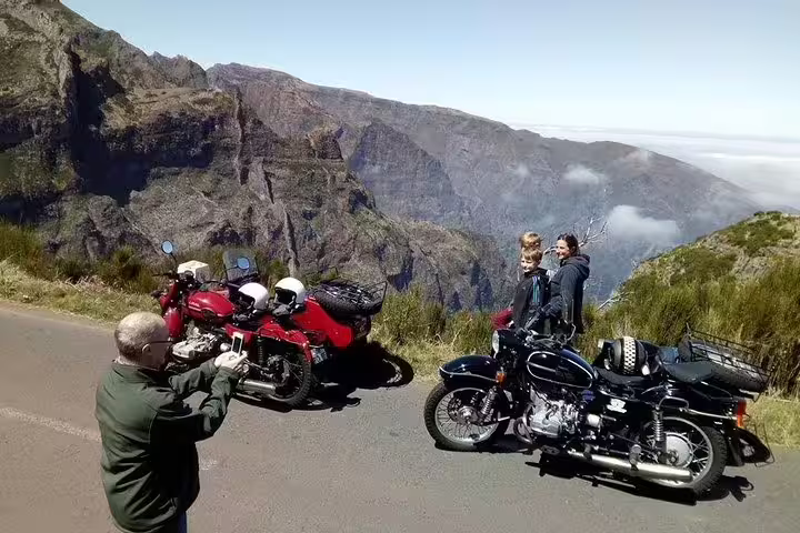 Tourists enjoy breathtaking mountain views during a Madeira Old Road West sidecar tour, capturing memories along scenic cliffs.