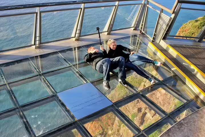 Visitors enjoying the breathtaking view from the glass-floored skywalk on Madeira's cliffs, part of the Skywalk Wonders tour.