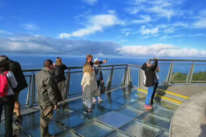 Tourists enjoy panoramic ocean views from a glass skywalk in Madeira, perfect for scenic adventures and 4x4 tours.