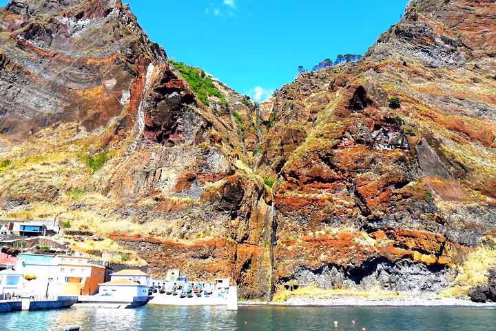 Dramatic volcanic cliffs tower over a small coastal harbor in Madeira on a guided caves and coastal tour