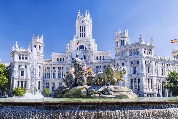 Cibeles Fountain and Palace in Madrid, Spain, with water jets and lion sculptures under blue sky