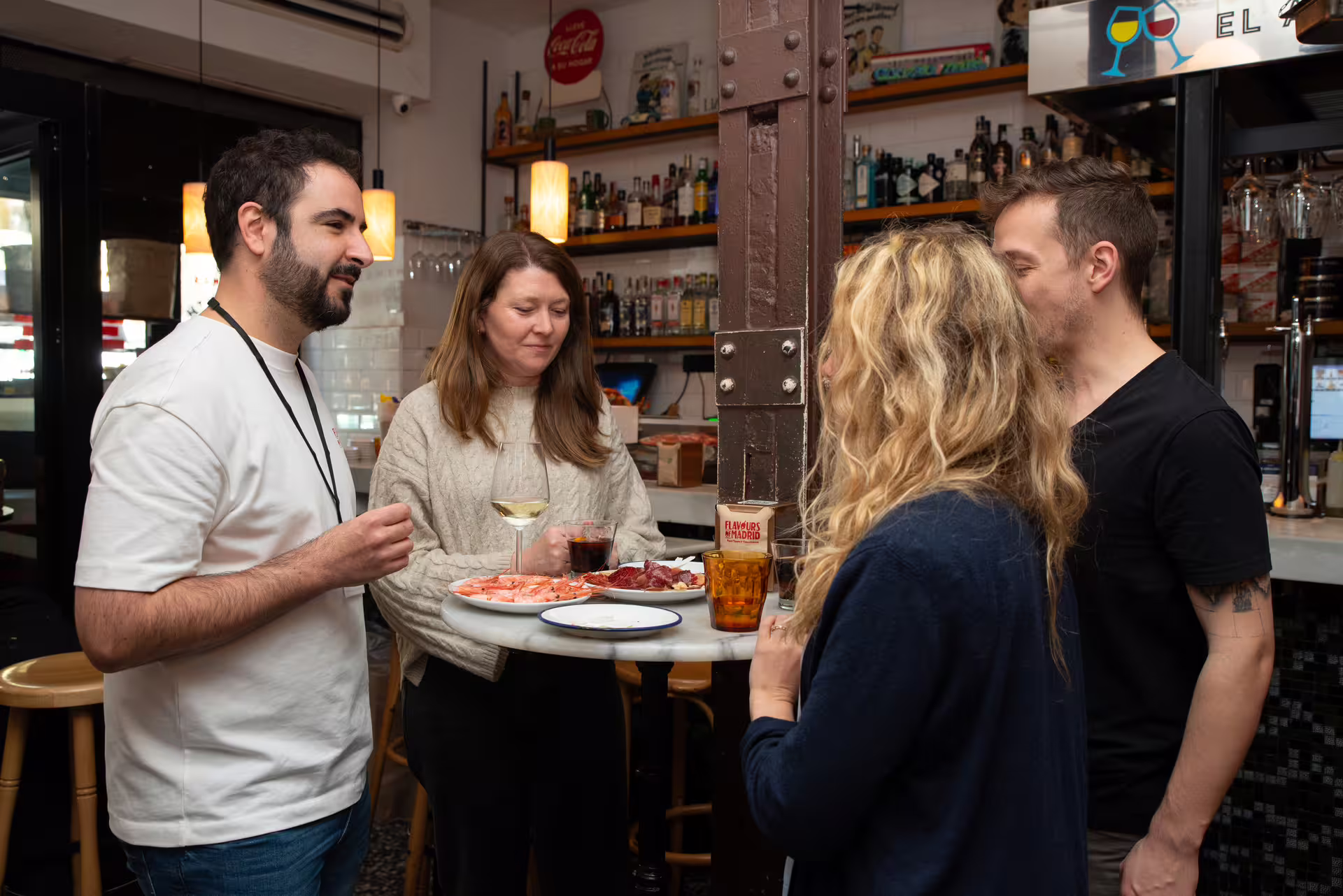 A group of tourists enjoy tapas and wine at a cozy bar during an authentic Madrid food and culture tour experience.