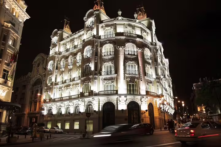 Ornate illuminated historic building facade in Madrid at night with cars passing by