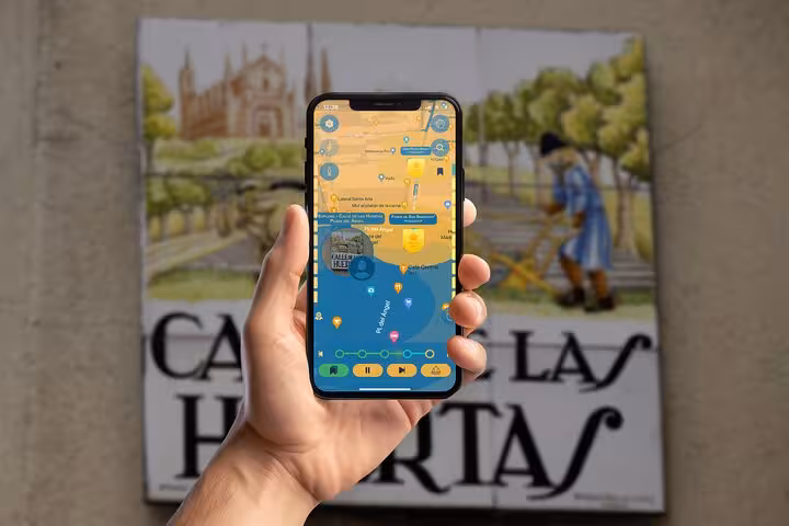 Interactive Madrid Golden Age history tour app on smartphone near Calle Las Huertas historic street mural