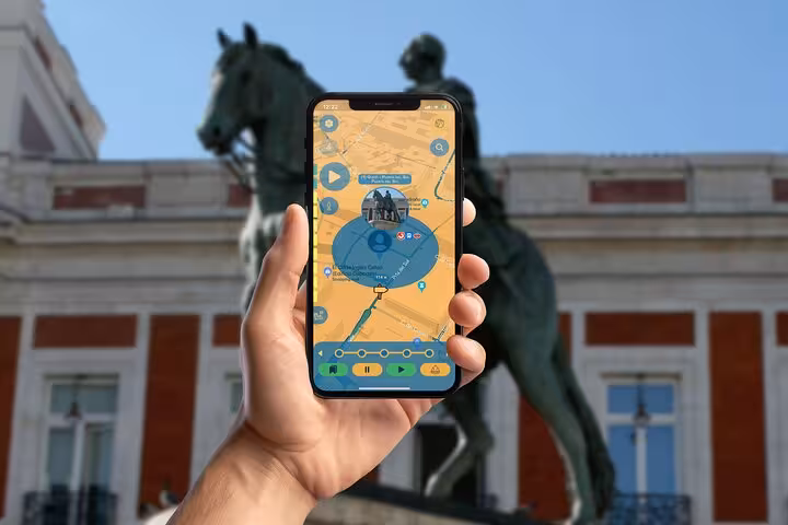 Hand holding smartphone with self-guided walking tour app map in front of Madrid's iconic equestrian statue at Puerta del Sol